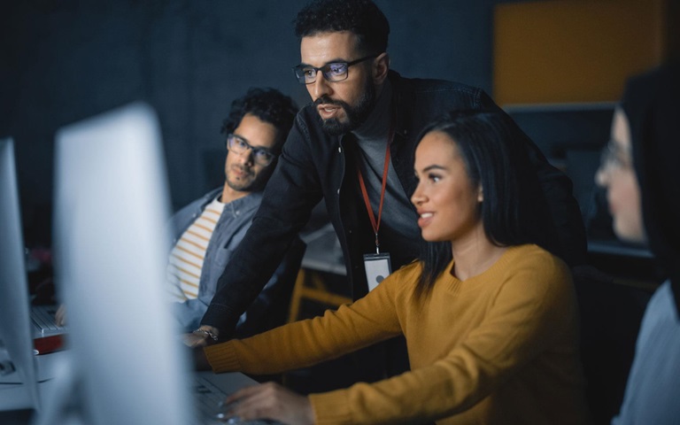 four business men and women looking at computer screen in dark room