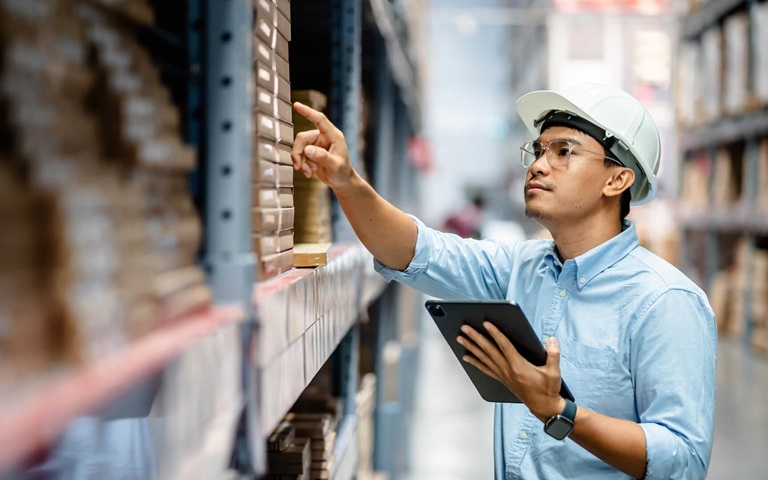 logistics worker in warehouse with hardhat and tablet in hand