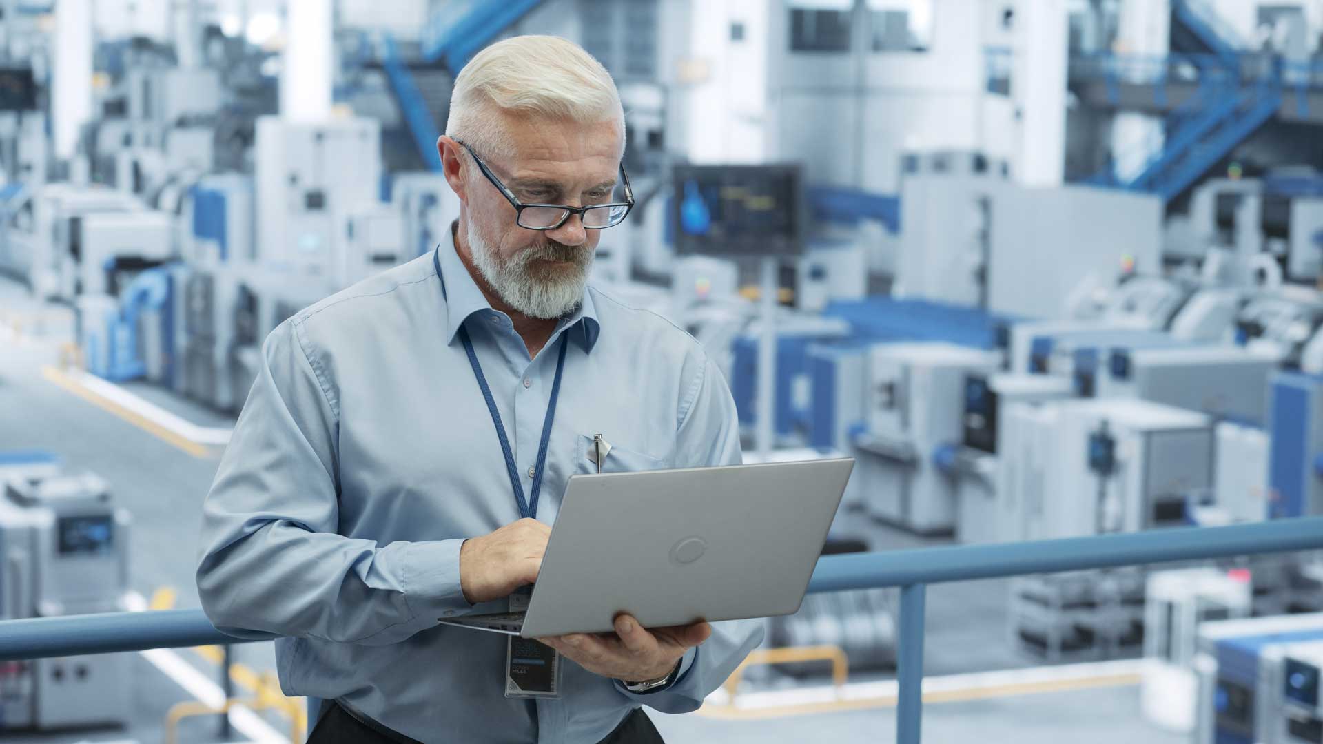 man holding an open laptop standing in a lab implementing new protocols for instrument quality control