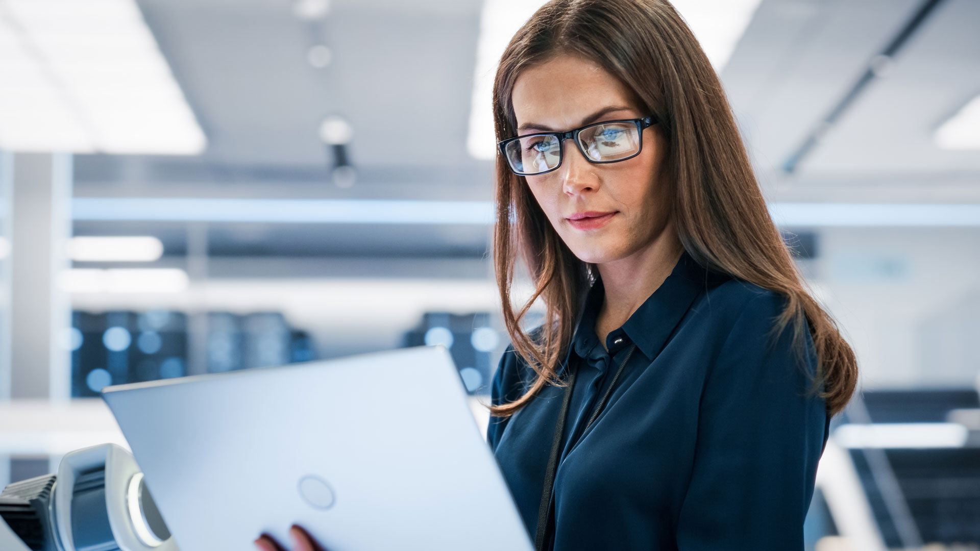 woman in business attire wearing glasses holding and gazing at her laptop